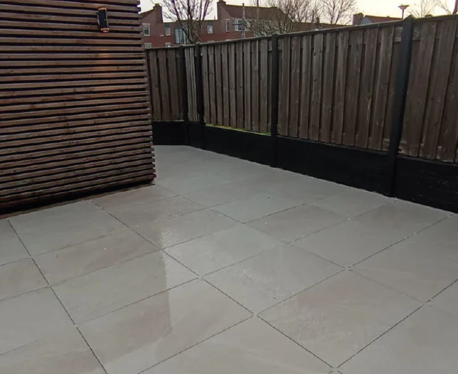 Nieuw aangelegd terras met lichtgrijze tegels en houten gevelbekleding.