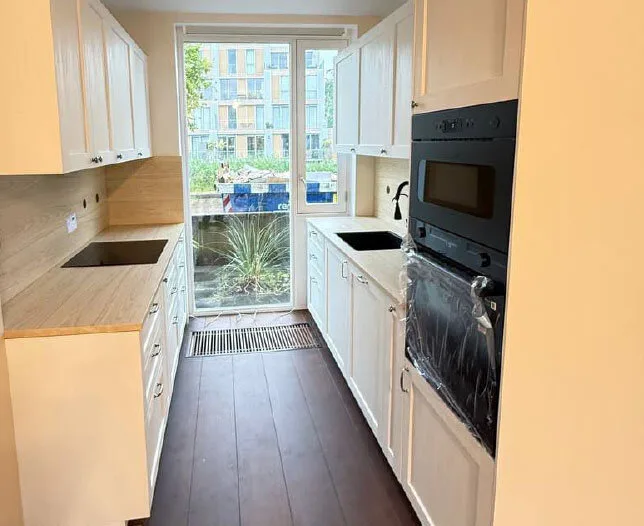 Nieuw gerenoveerde keuken met witte kasten, houten blad en inbouwapparatuur.